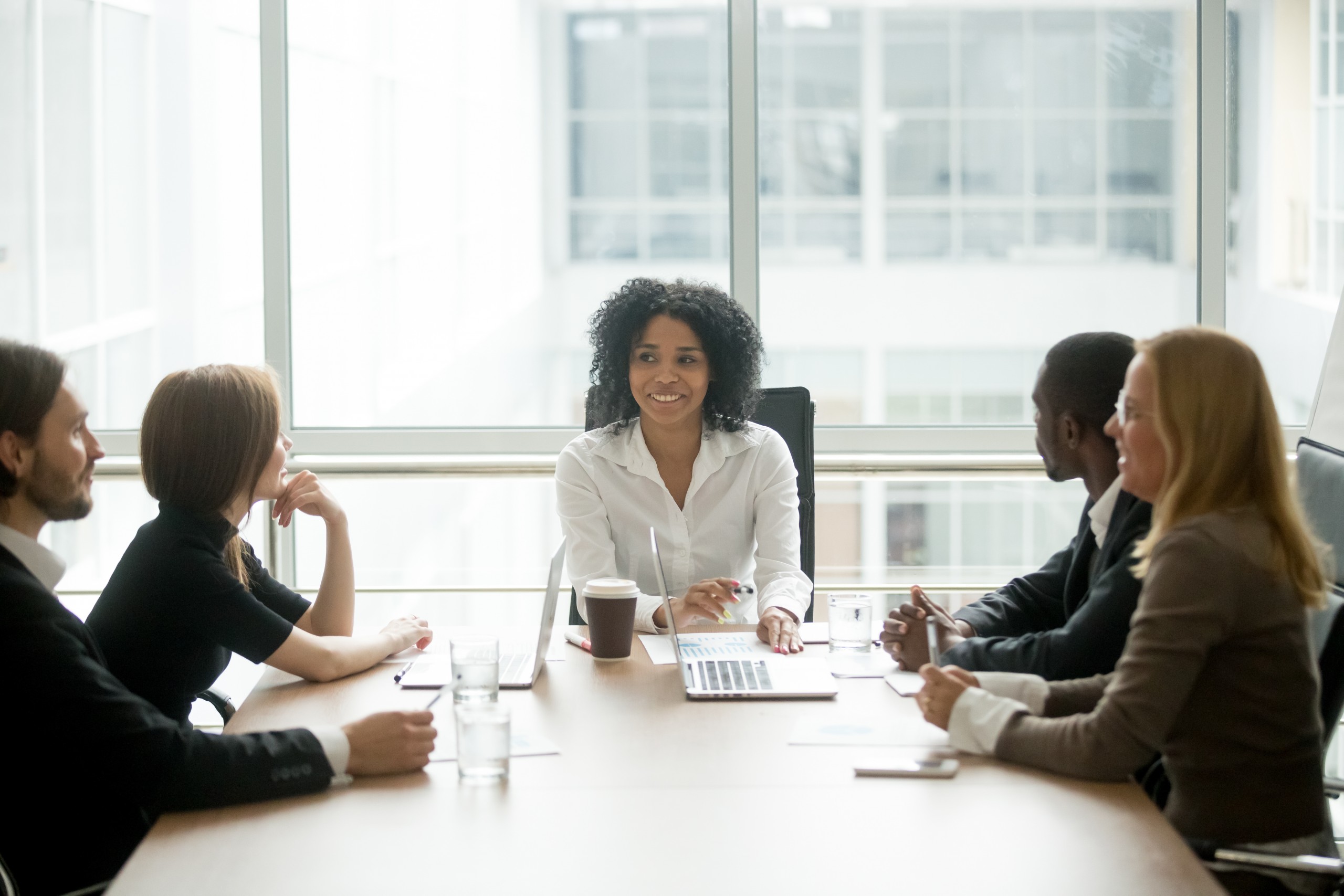Landing Page - Accelerate Market Access 2 Smiling friendly african female boss leading corporate diverse team meeting talking to multiracial partners employees discussing results or planning work at group multi-ethnic briefing in boardroom