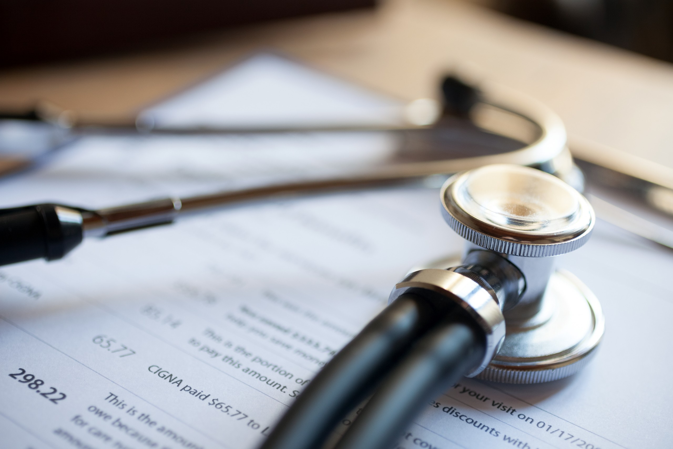 Insurance reimbursement paperwork on a clipboard under a stethoscope.
